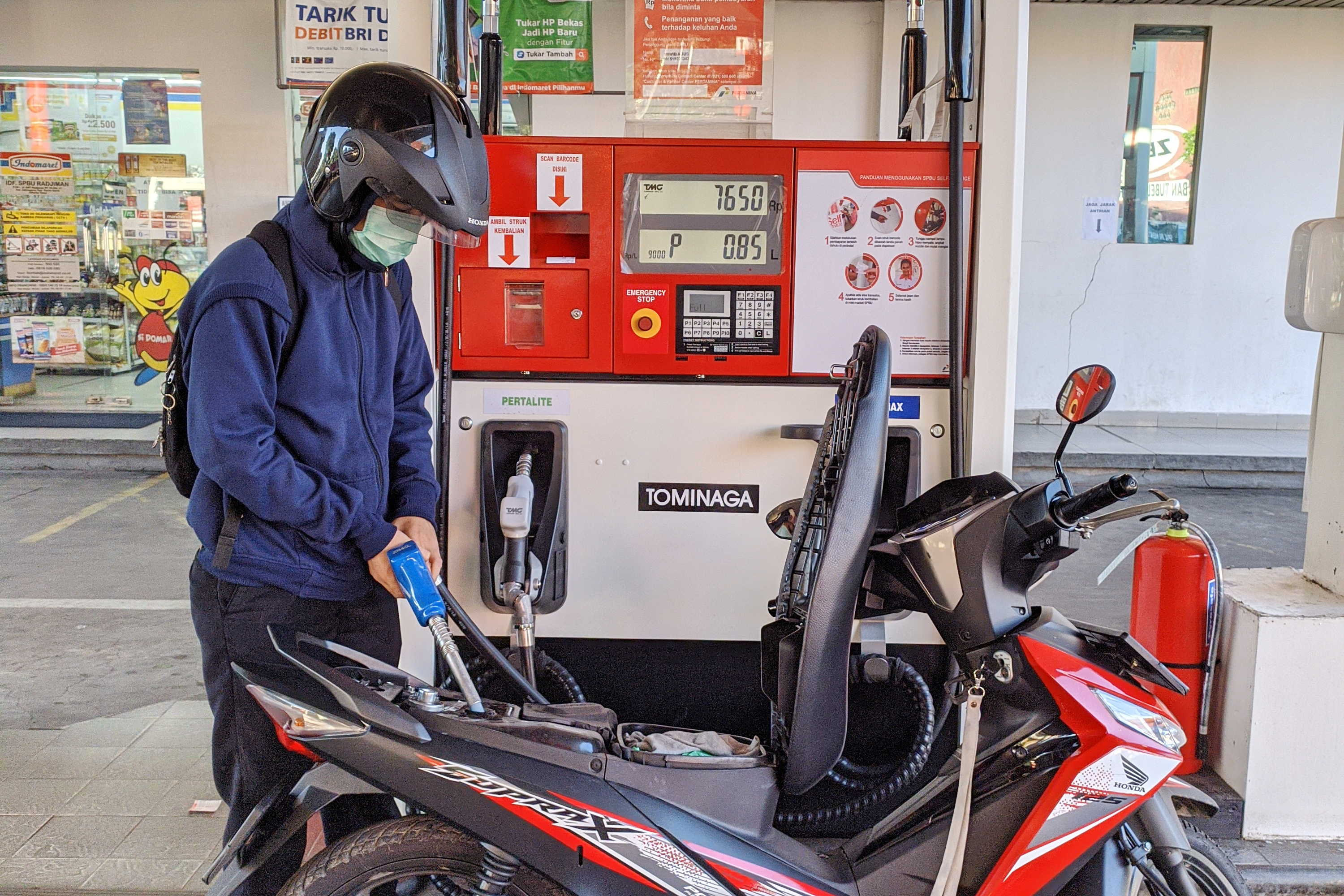 Jakarta gas pump with a masked man filling his bike up. 